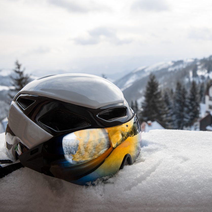 Ski helmet with reflective colors googles in snow with mountain hills in background. Copy space